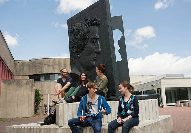Studierende sitzen am Heinrich Heine Denkmal