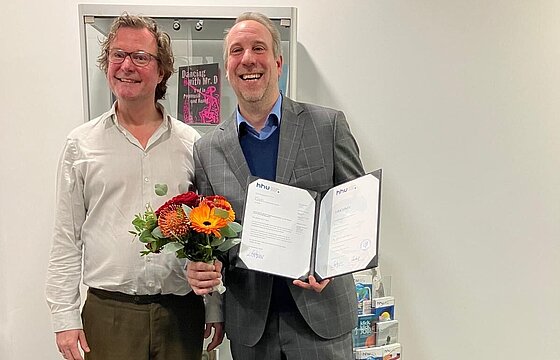 Prodekan Prof. Dr. Roger Lüdeke seht links neben Prof. Dr. Frank Meier. Frank Meier hält einen Blumenstrauß und seine Ernennungsurkunde in den Händen.