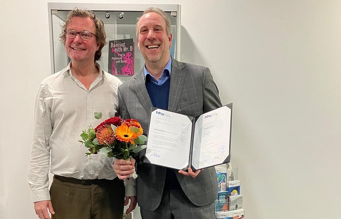 Prodekan Prof. Dr. Roger Lüdeke seht links neben Prof. Dr. Frank Meier. Frank Meier hält einen Blumenstrauß und seine Ernennungsurkunde in den Händen.