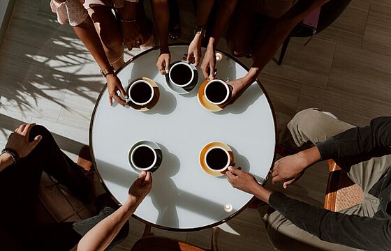 Fünf Kaffeetassen auf und mehrere Personen um einen Tisch