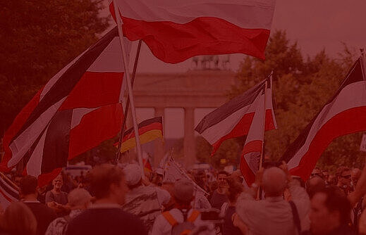 Menschen mit wehenden Deutschlandfahnen vor dem Brandenburger Tor. Über dem Bild ist ein roter Filter.