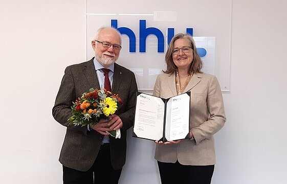  von links: apl.-Dr. Mikhail Boytsov und Dekanin Prof. Dr. Ulli Seegers stehen vor dem blauen HHU-Schild