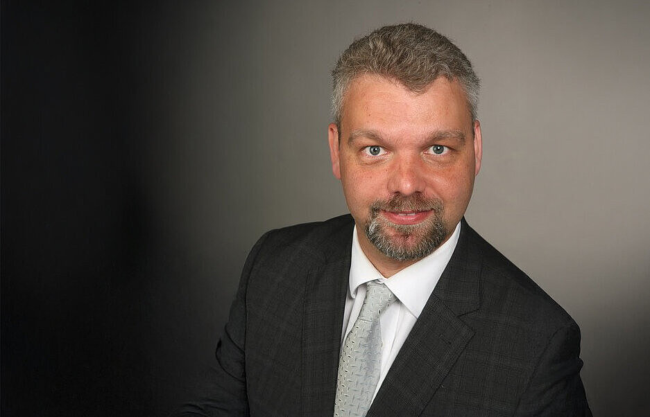 Eine Person im Anzug vor einem dunklen Hintergrund