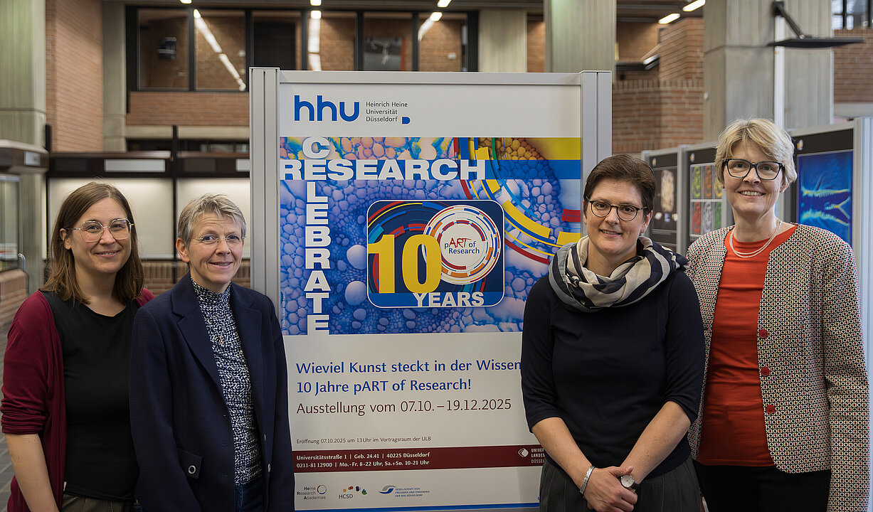 Vier Frauen im Gebäude der Universitätsbibliothek vor dem Plakat zur Kalenderausstellung