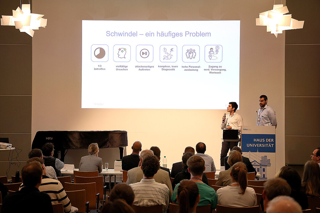 Das Team Vertigo auf der Bühne des Pitch4MED. Die Pitch-Präsentation ist eingeblendet.