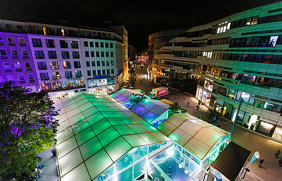 Blick auf das bunt beleuchtete Aktionszelt auf dem abendlichen Düsseldorfer Schadowplatz