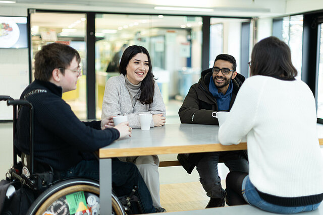 Vier Studierende sitzen an einem Tisch im Bereich der Cafeteria.