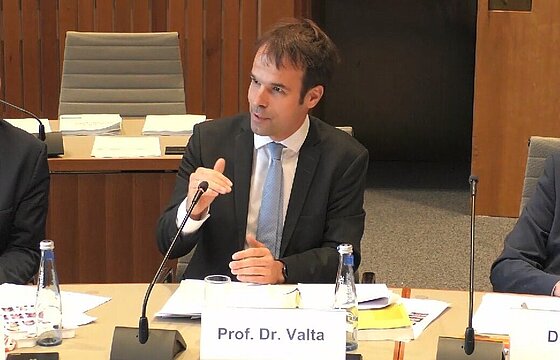 Prof. Dr. Matthias Valta, sitzend, hinter einem Namensaufsteller, vor sich ein Tischmikrophon