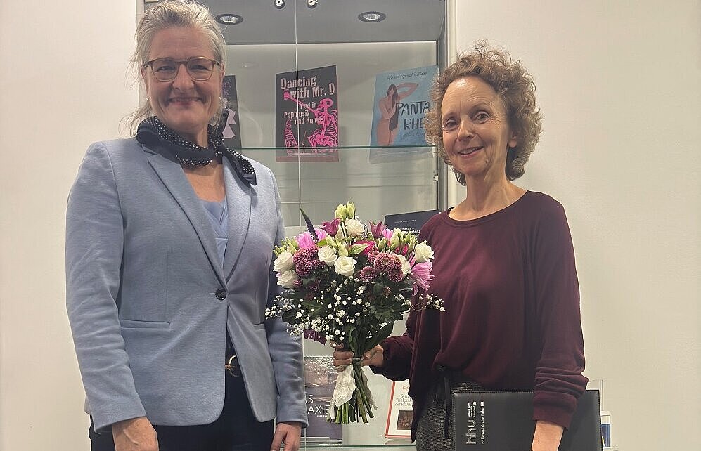 Dekanin Prof.-Dr. Ulli Seegers steht links neben apl.-Prf. Dr. Martina Nicklaus. Martina Nicklaus hat einen Blumenstrauß in der Hand.