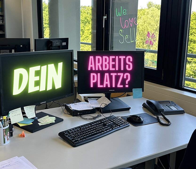 Ein Schreibtisch in einem Büro mit Ausblick ins Grüne, auf den Bildschirmen steht: Dein Arbeitsplatz?