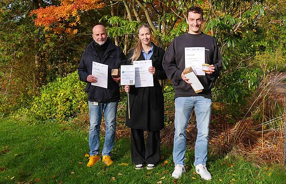 Drei Personen mit Urkunden im Botanischen Garten der HHU.